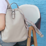 Light gray cowhide leather women's backpack with belt decoration and zipper buckle on chair.