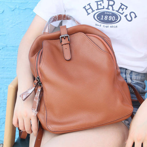 Women's fashion brown cowhide leather backpack with belt decoration and zipper buckle displayed on lap