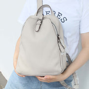 Light gray top layer cowhide leather backpack with belt decoration and zipper, worn by a person in casual outfit.