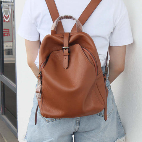 Woman wearing a brown leather backpack with buckle, showcasing medium-sized top layer cowhide design, perfect for casual fashion.